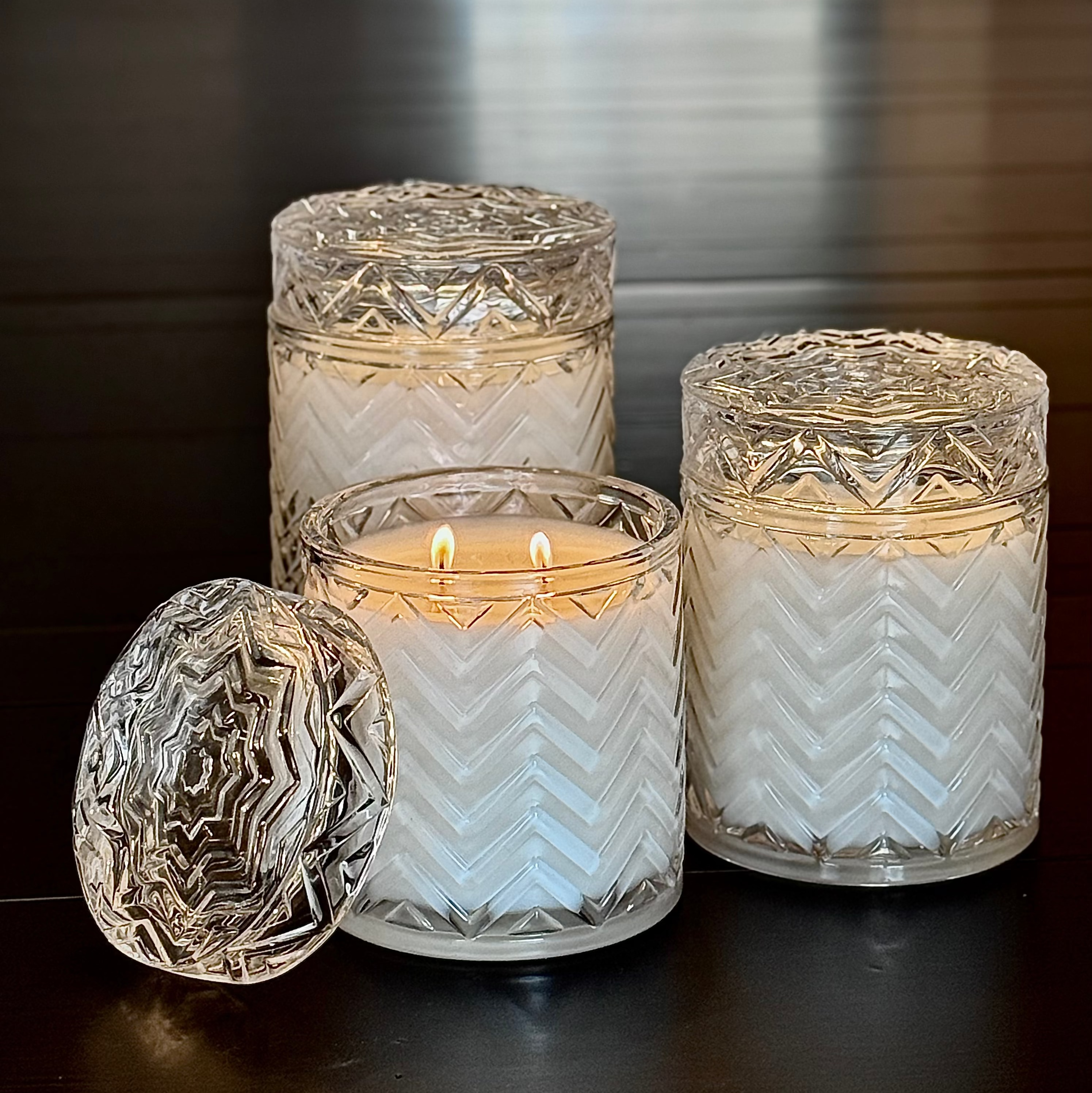 Set of three glass candle holders with a lit candle on a reflective surface